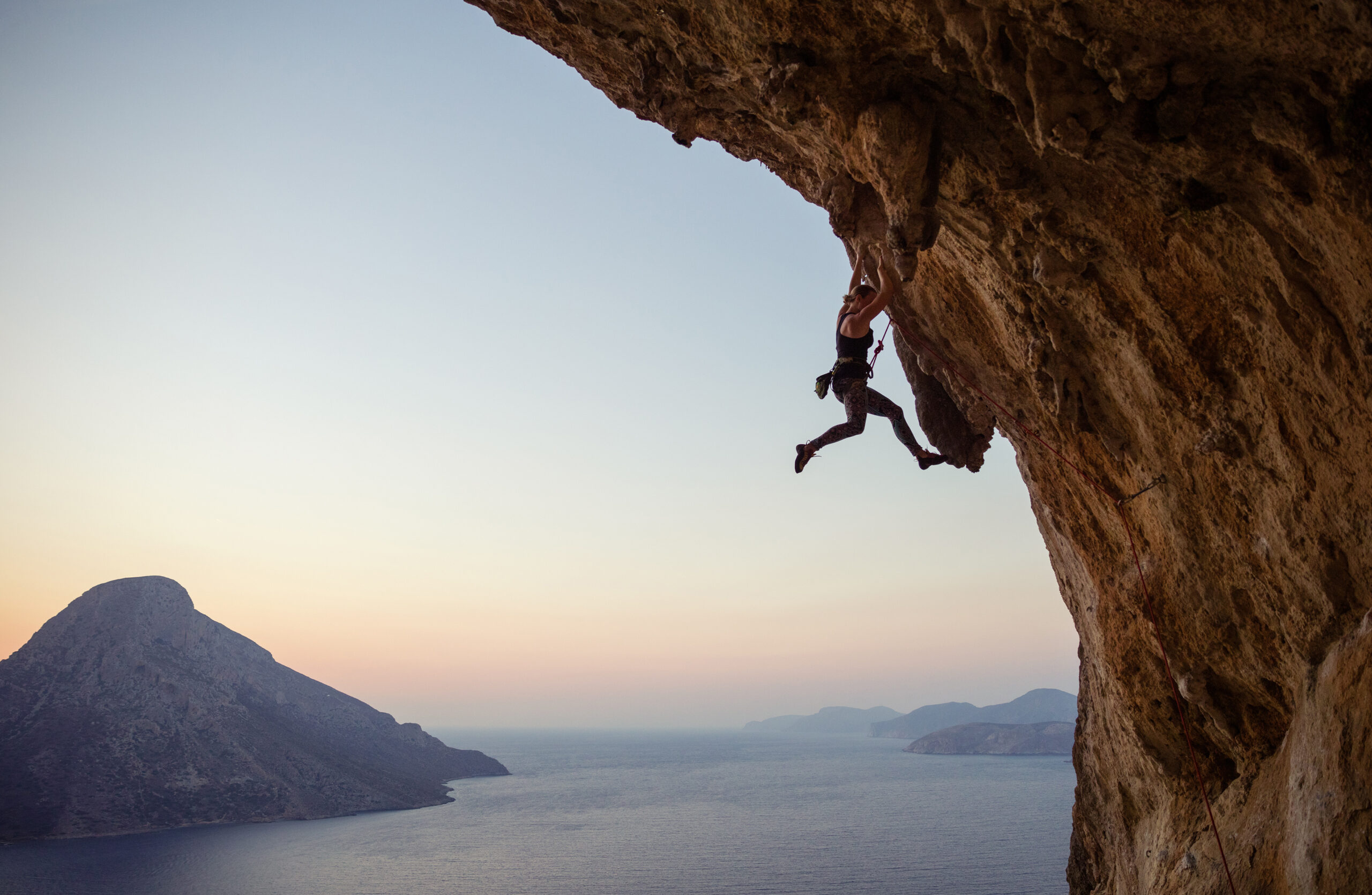 Young woman climbing challenging route at sunset